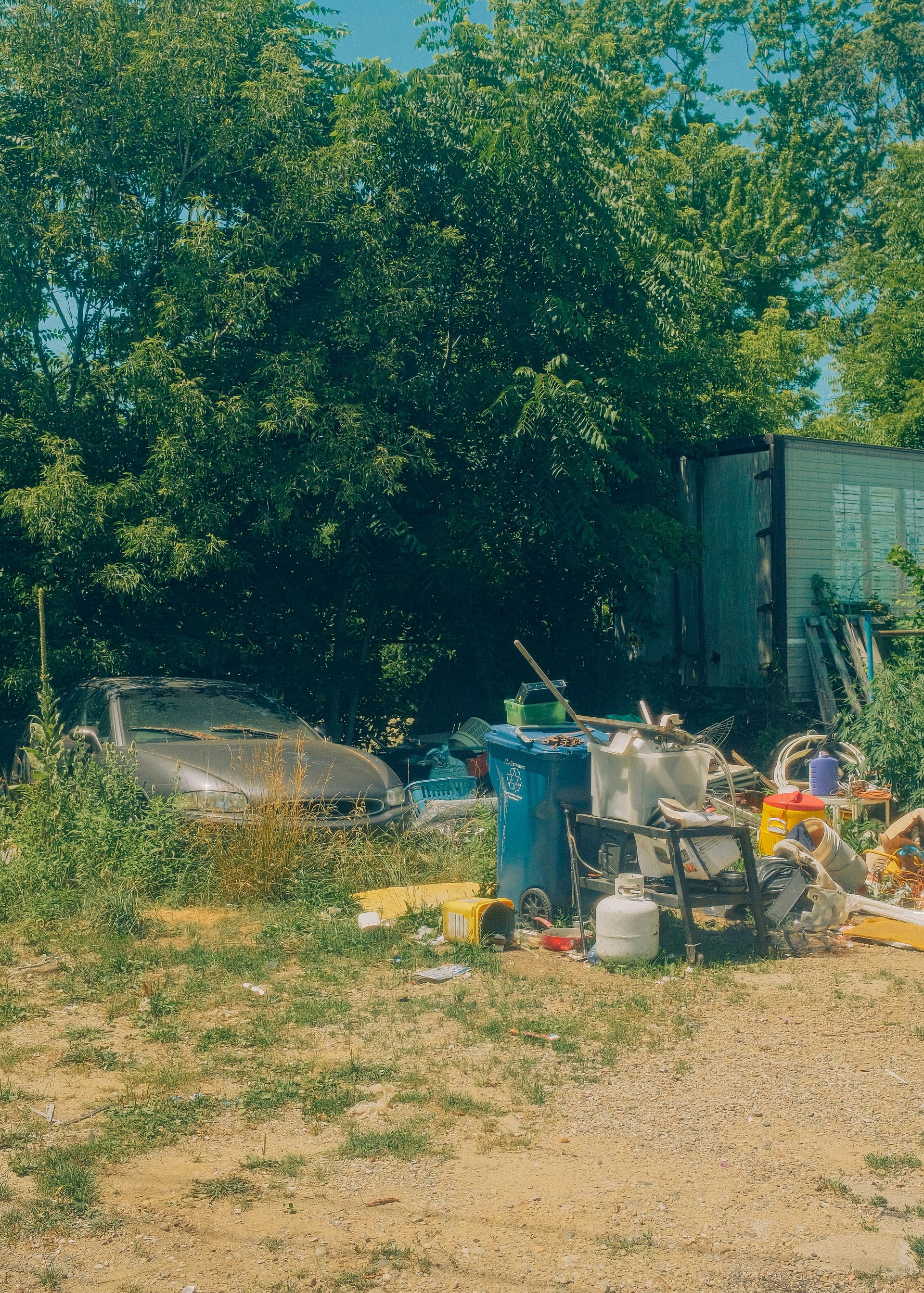 Abandoned car and scattered trash in an overgrown outdoor lot